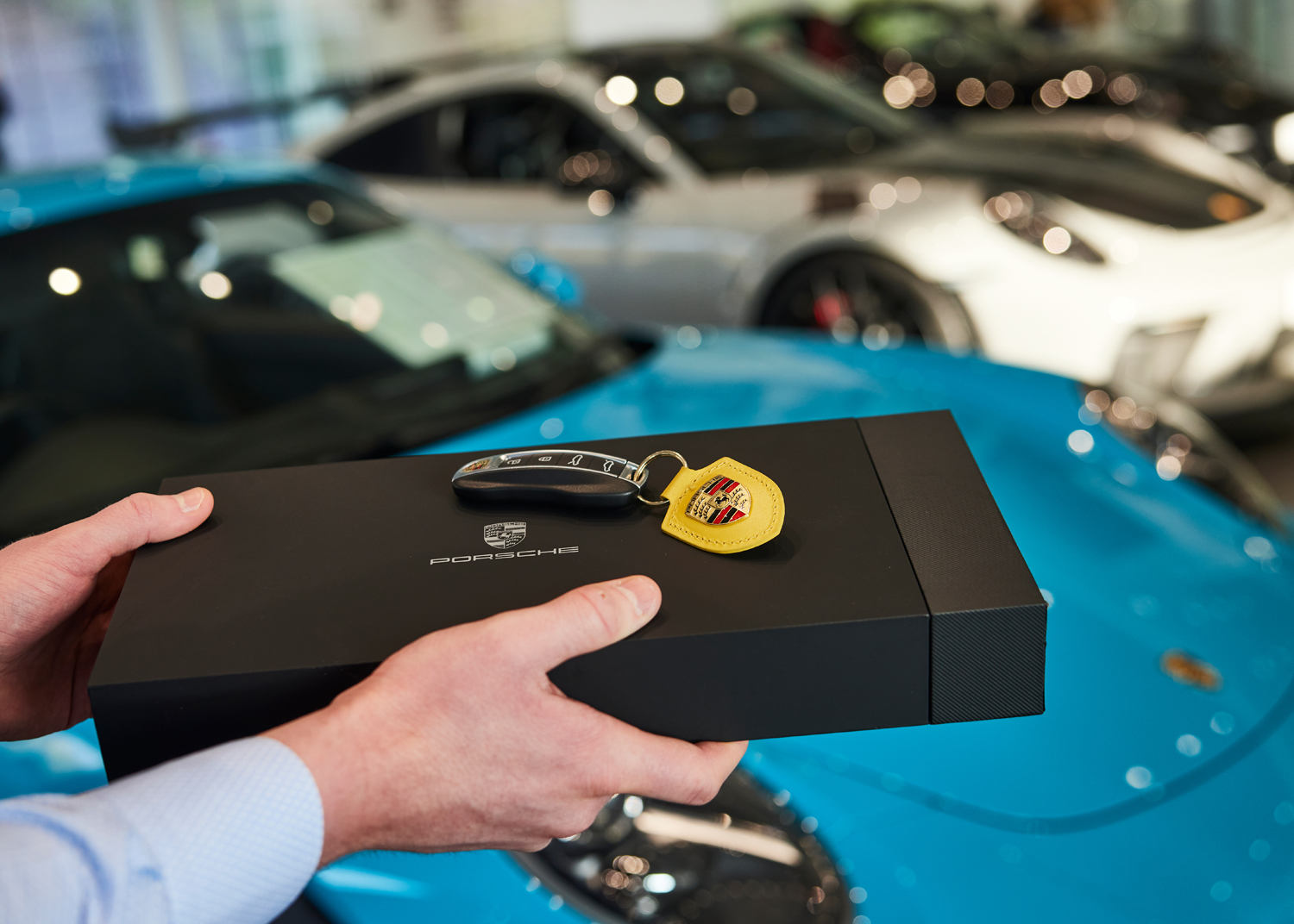 Porsche presentation pack handed over beside a blue Porsche