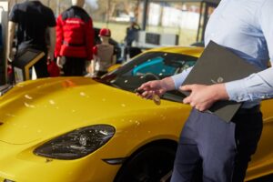 Car dealer handing over the keys to a new car in the showroom, holding a branded handover folder