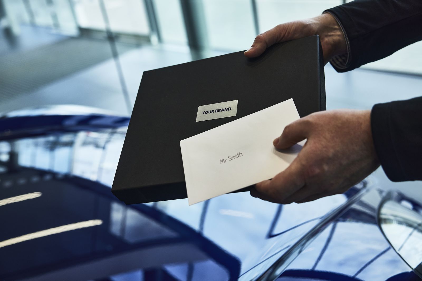 Salesperson handing over a branded Silverstone box and a personalised envelope beside a new car